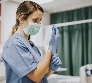 A healthcare worker with a mask is putting on gloves