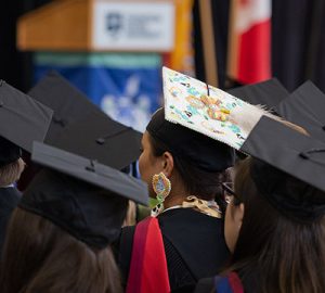 A colourful graduation cap stands out in a sea of black caps