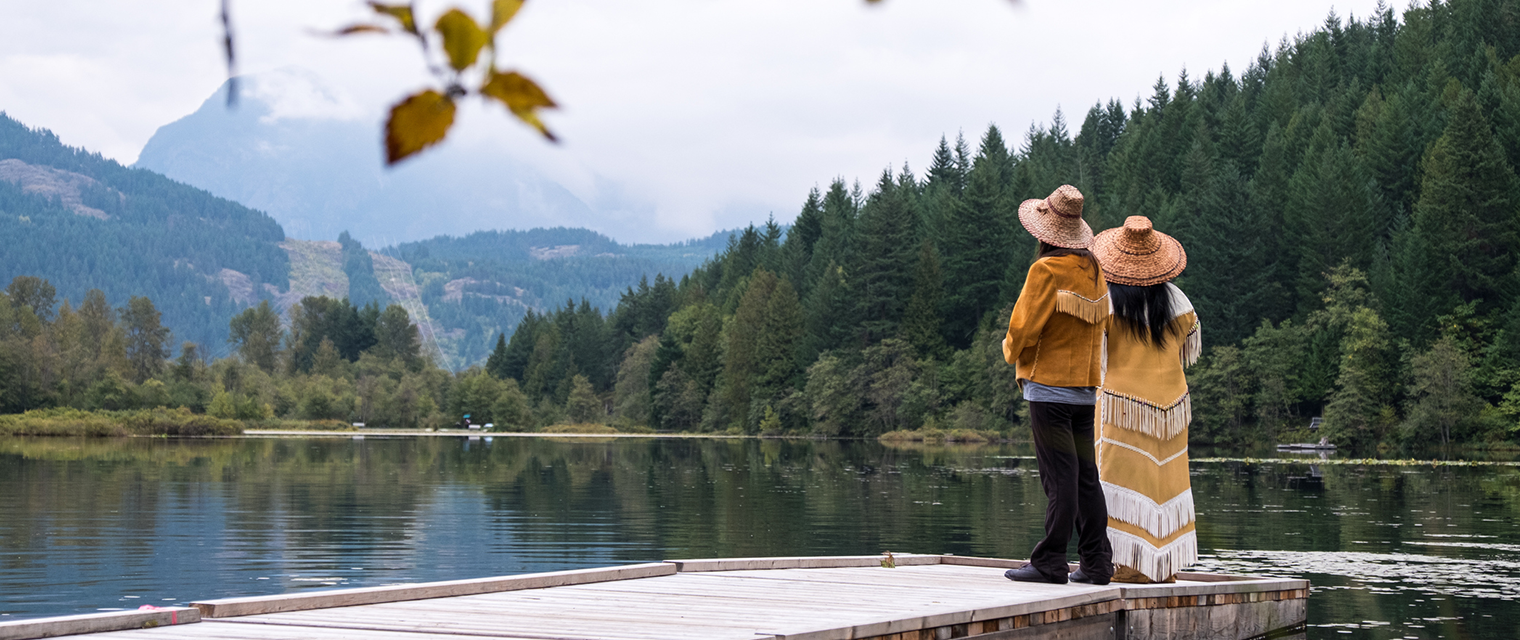 Two individuals standing on a dock looking at the water and landscape